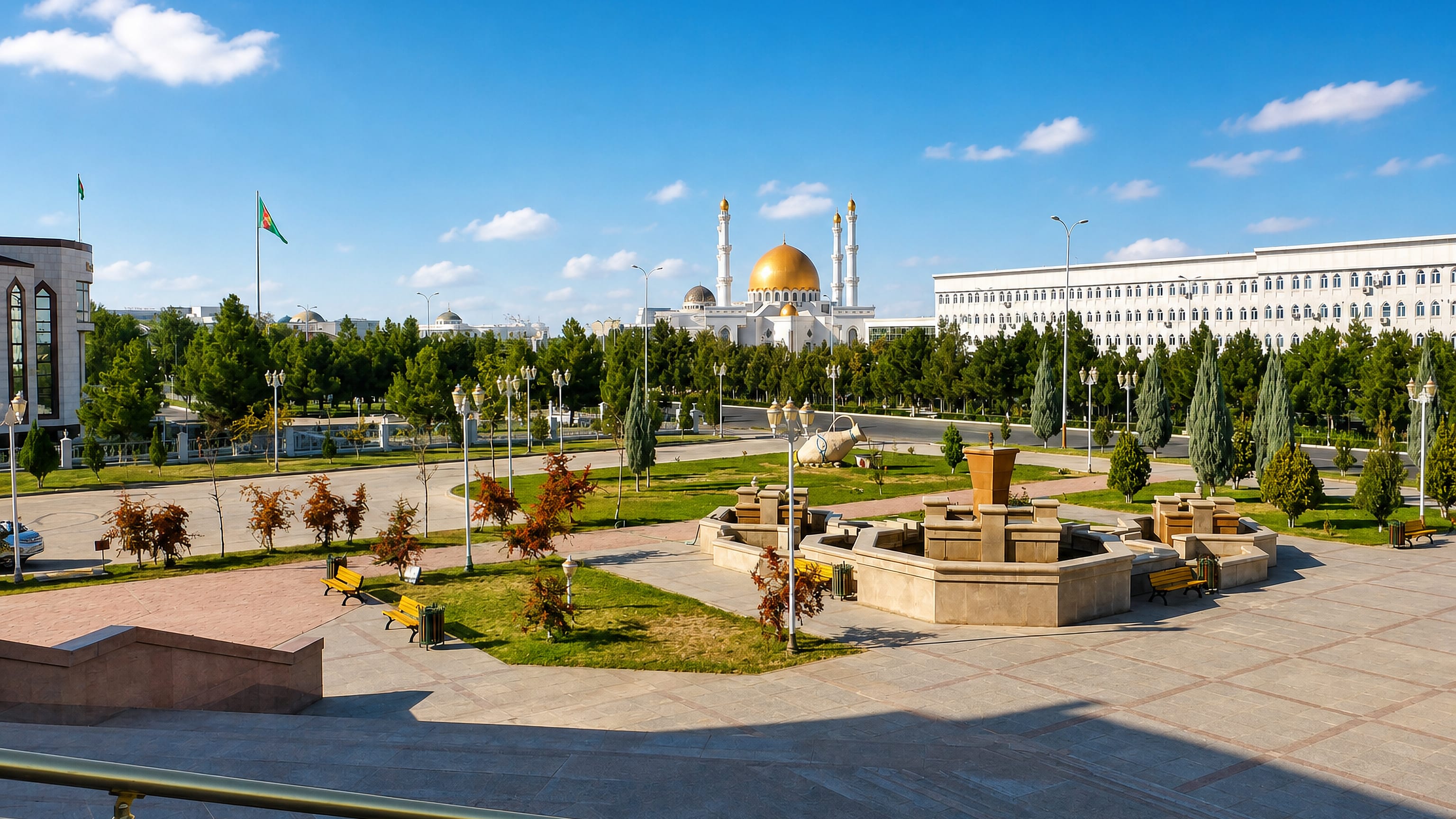 White marble civic buildings and a gold-domed mosque across a landscaped plaza in Mary, Turkmenistan.