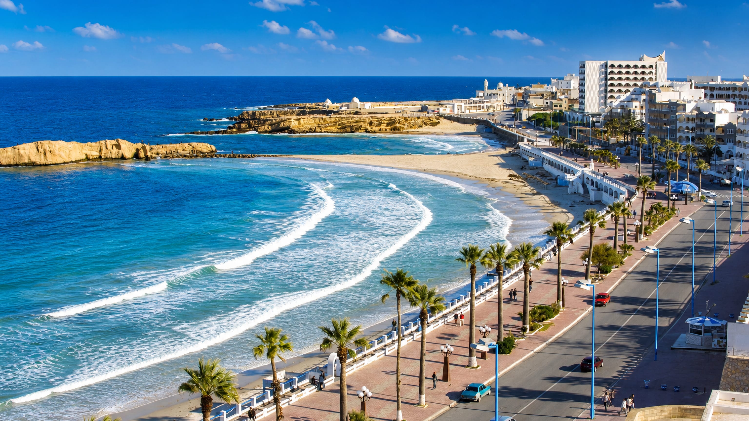 Palm-lined corniche promenade curving along Monastir's sandy bay on Tunisia's Mediterranean coast.