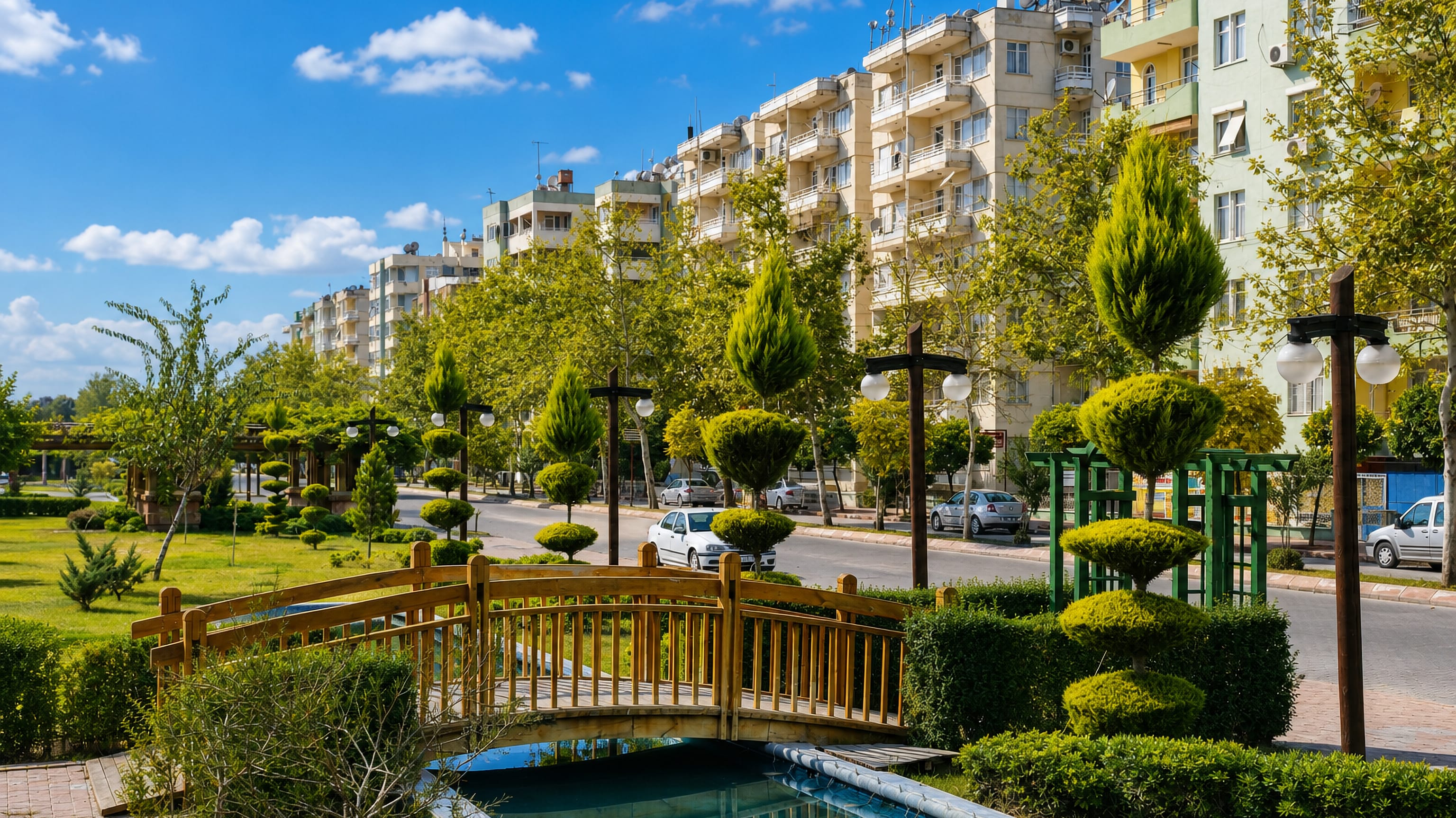 Landscaped park with a wooden footbridge and clipped topiary below apartment blocks in Ceyhan, Turkey.
