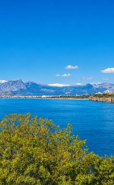 Antalya coastline with turquoise sea, clifftop city, and the snow-capped Taurus Mountains behind