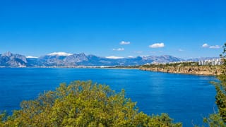 Antalya coastline with turquoise sea, clifftop city, and the snow-capped Taurus Mountains behind