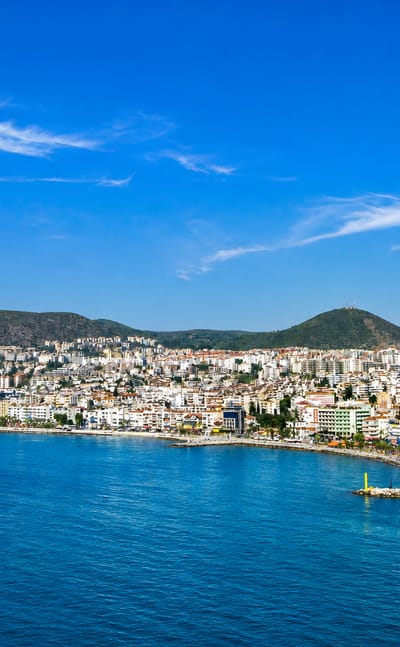 Kuşadası's white town curving around its Aegean bay with green hills behind and deep blue sea in front