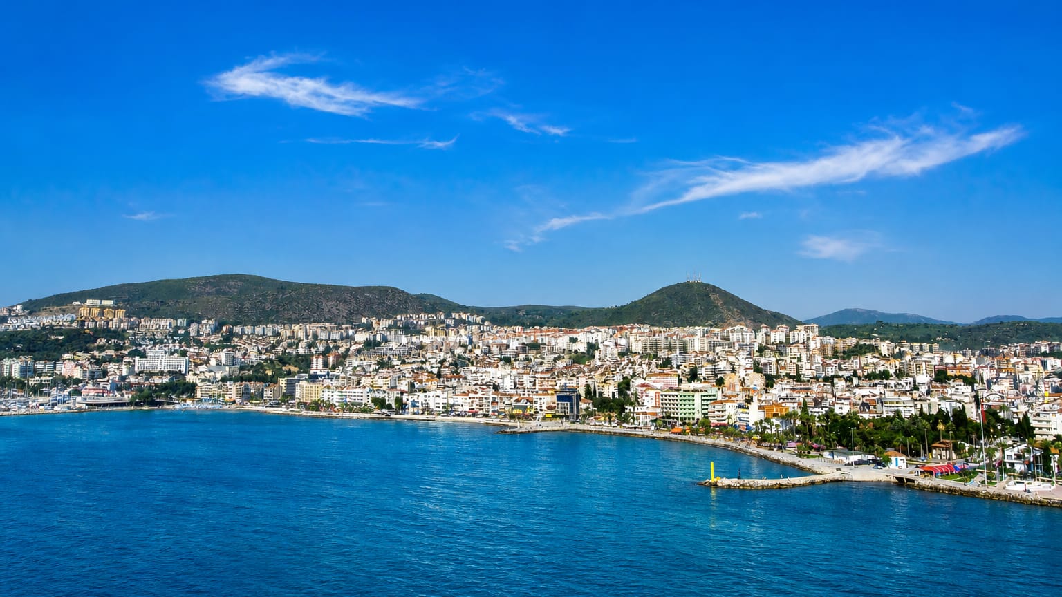 Kuşadası's white town curving around its Aegean bay with green hills behind and deep blue sea in front