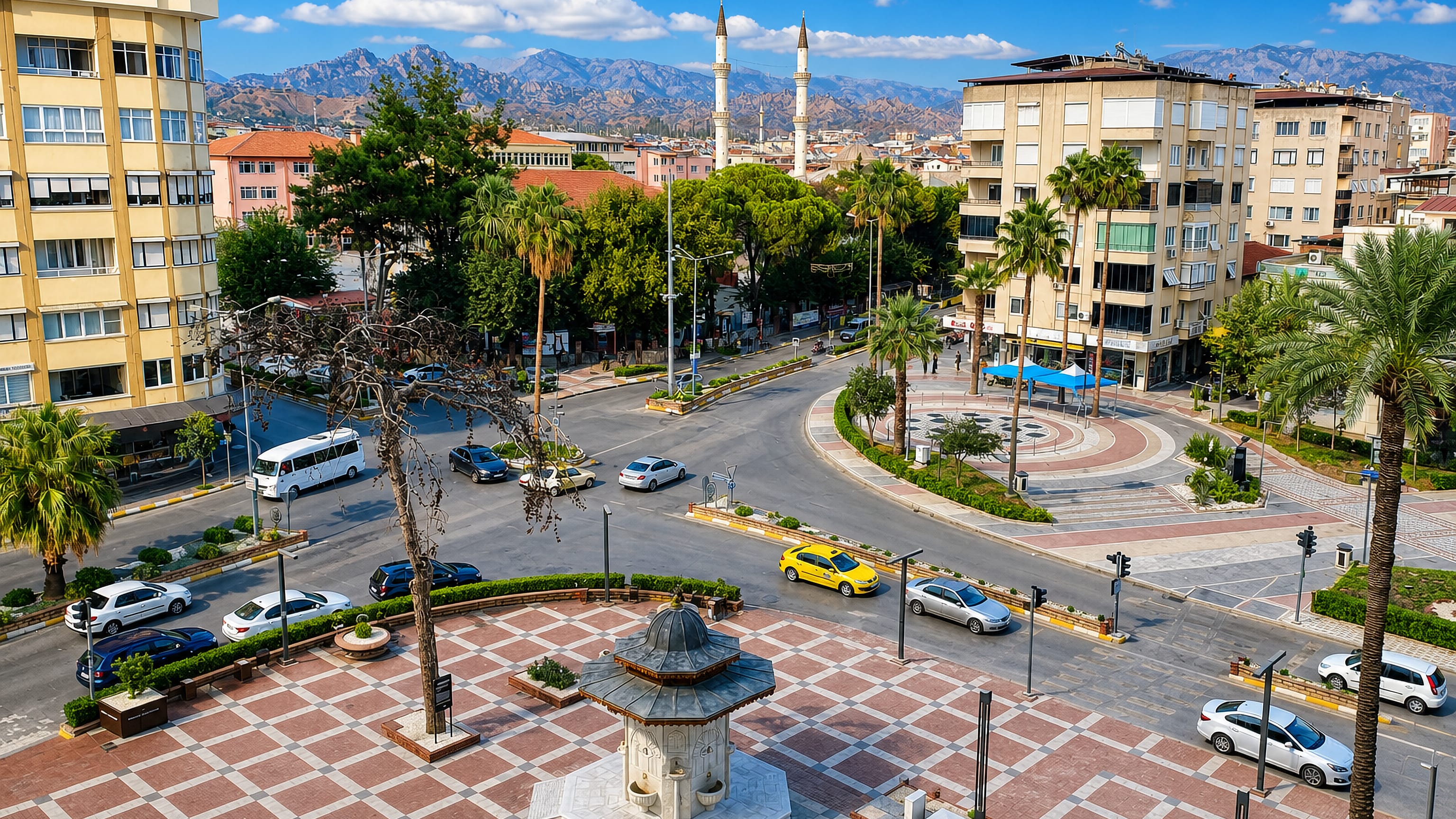 Central square in Nazilli, Turkey, with a stone fountain kiosk, palms and mosque minarets against the hills.