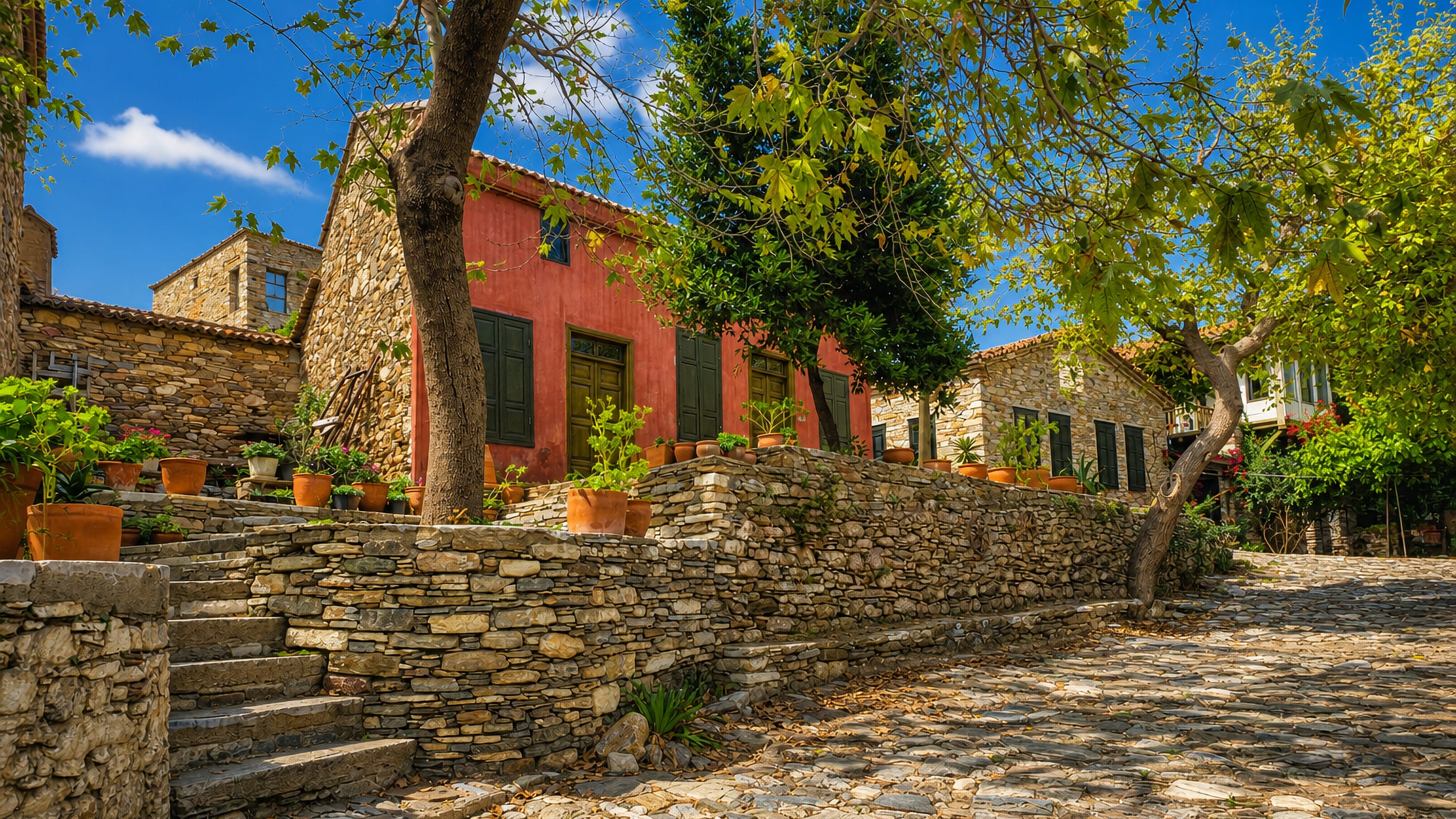 Stone-walled lane with a red-washed village house and potted plants in Söke, Aydın Province, Turkey.