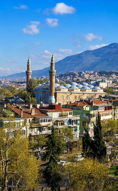 Bursa cityscape with the Grand Mosque's twin minarets below the snow-capped Uludag mountains