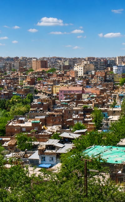 Rooftops of Diyarbakır's dense old town with a stone minaret and low brick houses under blue sky