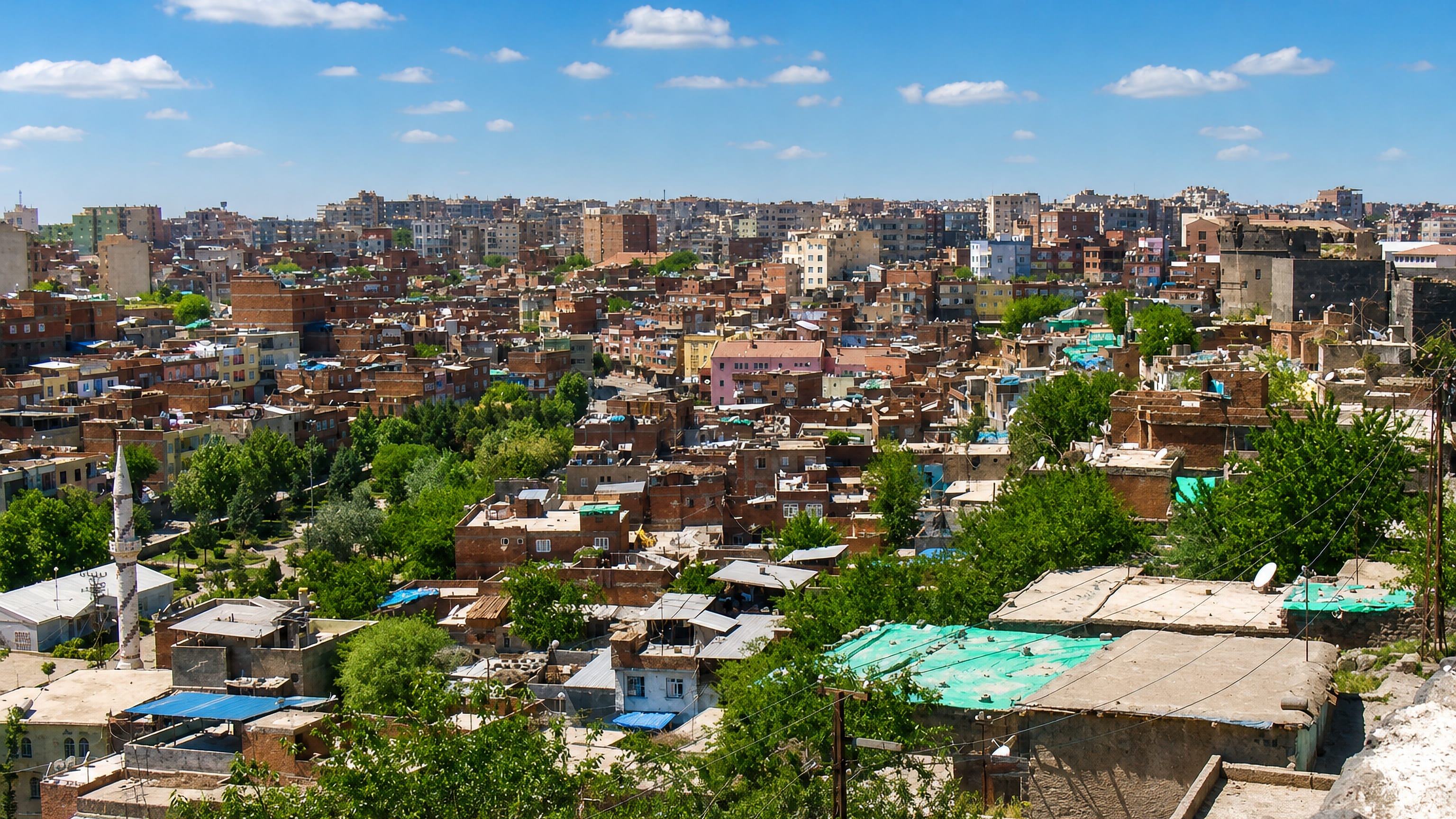 Rooftops of Diyarbakır's dense old town with a stone minaret and low brick houses under blue sky