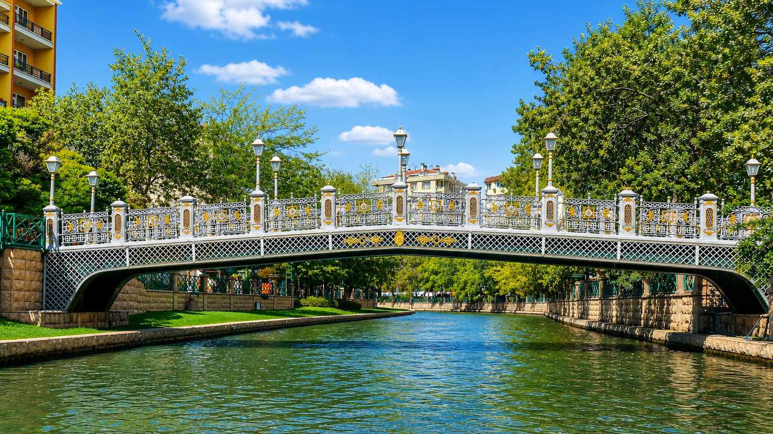 Ornate white iron footbridge over the Porsuk River canal in Eskişehir, framed by leafy green trees