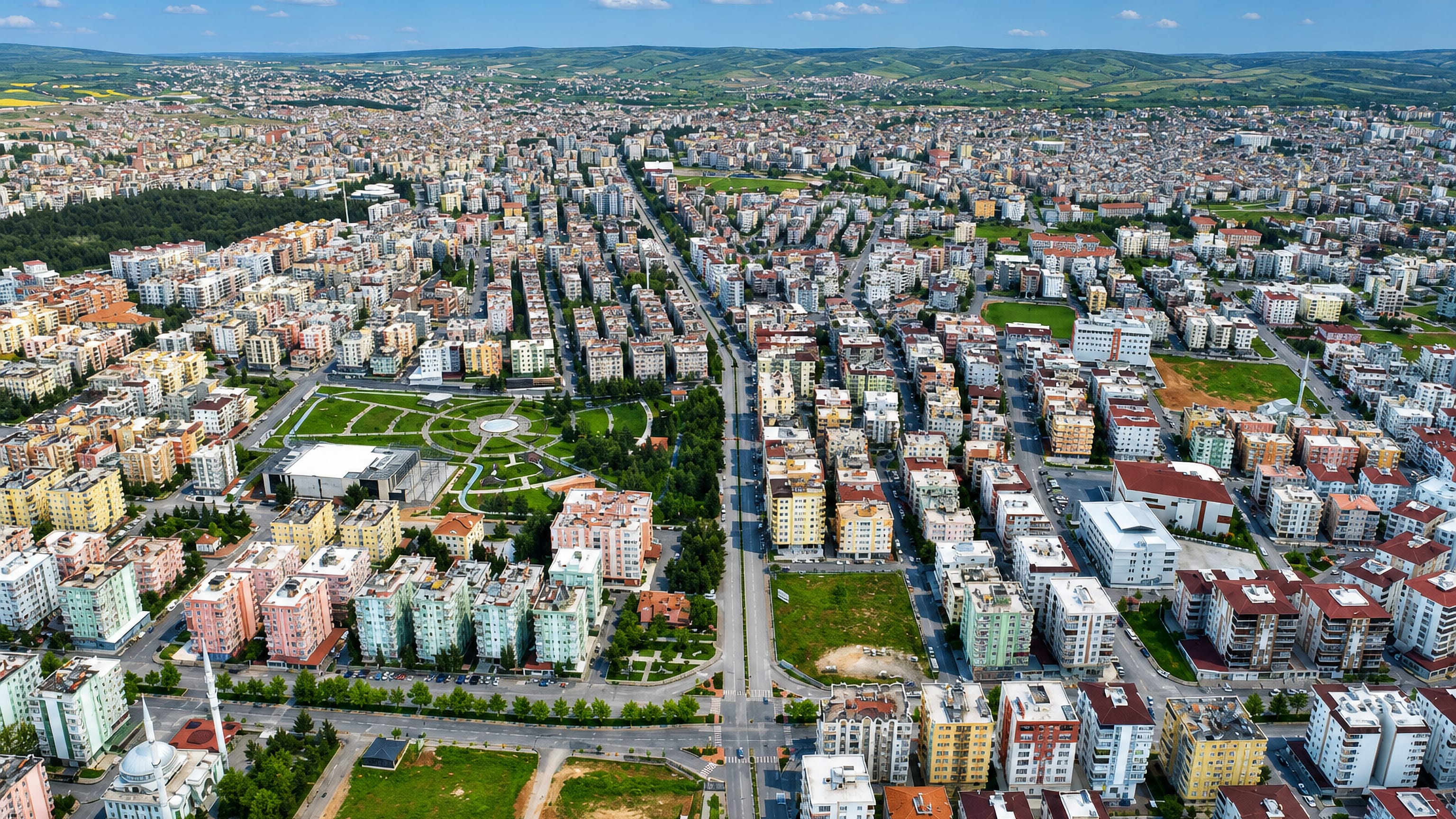 Aerial view of Nizip, Gaziantep, with a broad central boulevard, apartment blocks and rolling hills.