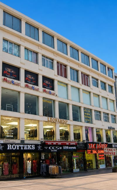 Street view of a multi-storey commercial building lined with textile shopfronts on a plaza in Laleli, Istanbul.