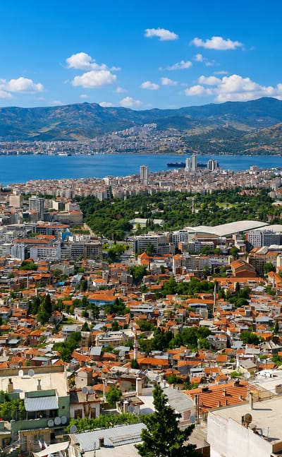 Aerial view of İzmir's red-roofed cityscape along its bay with mountains and port cranes beyond