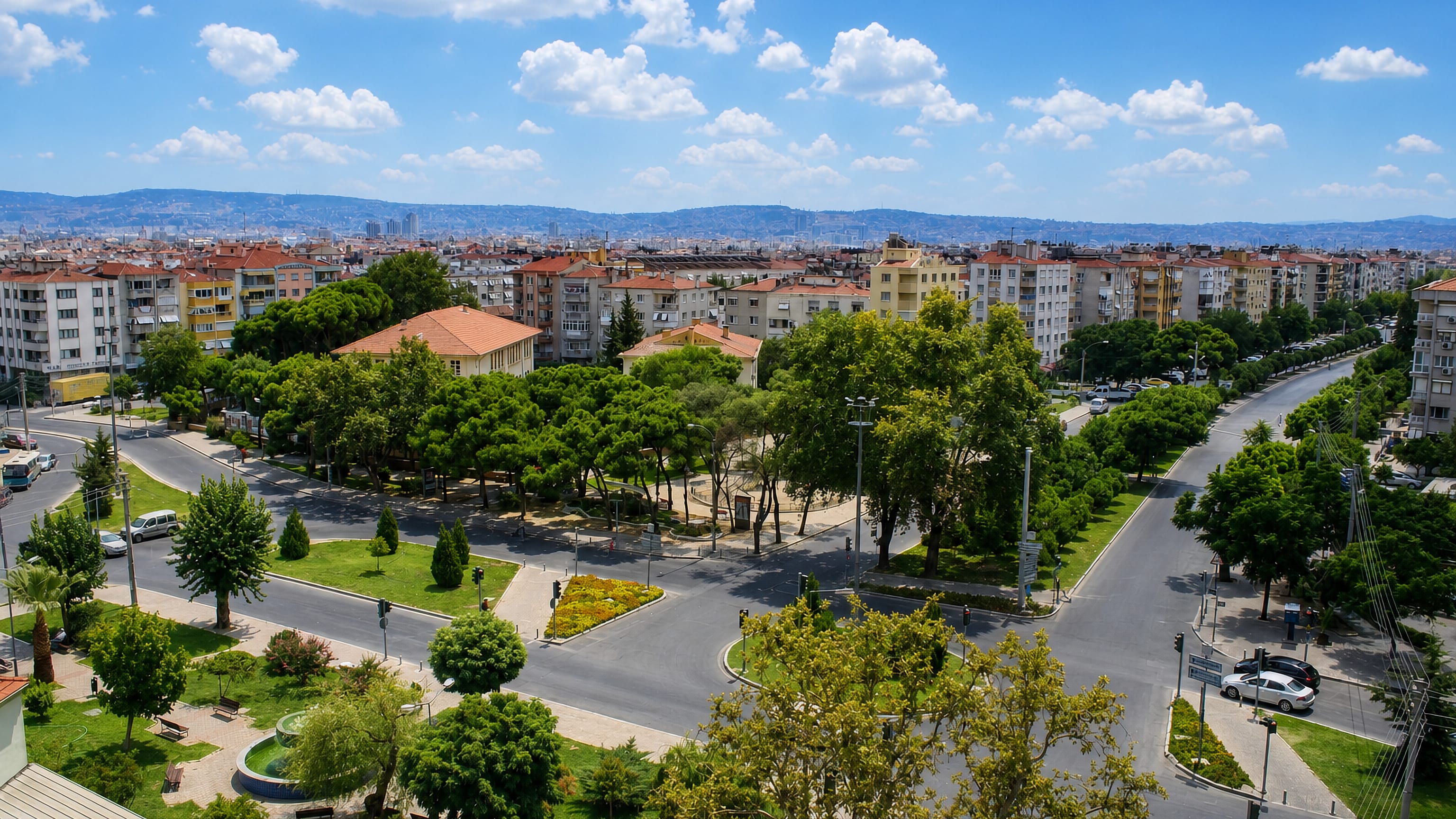 Aerial view over Karşıyaka's apartment blocks, tree-lined boulevards and park, with İzmir's hills behind.