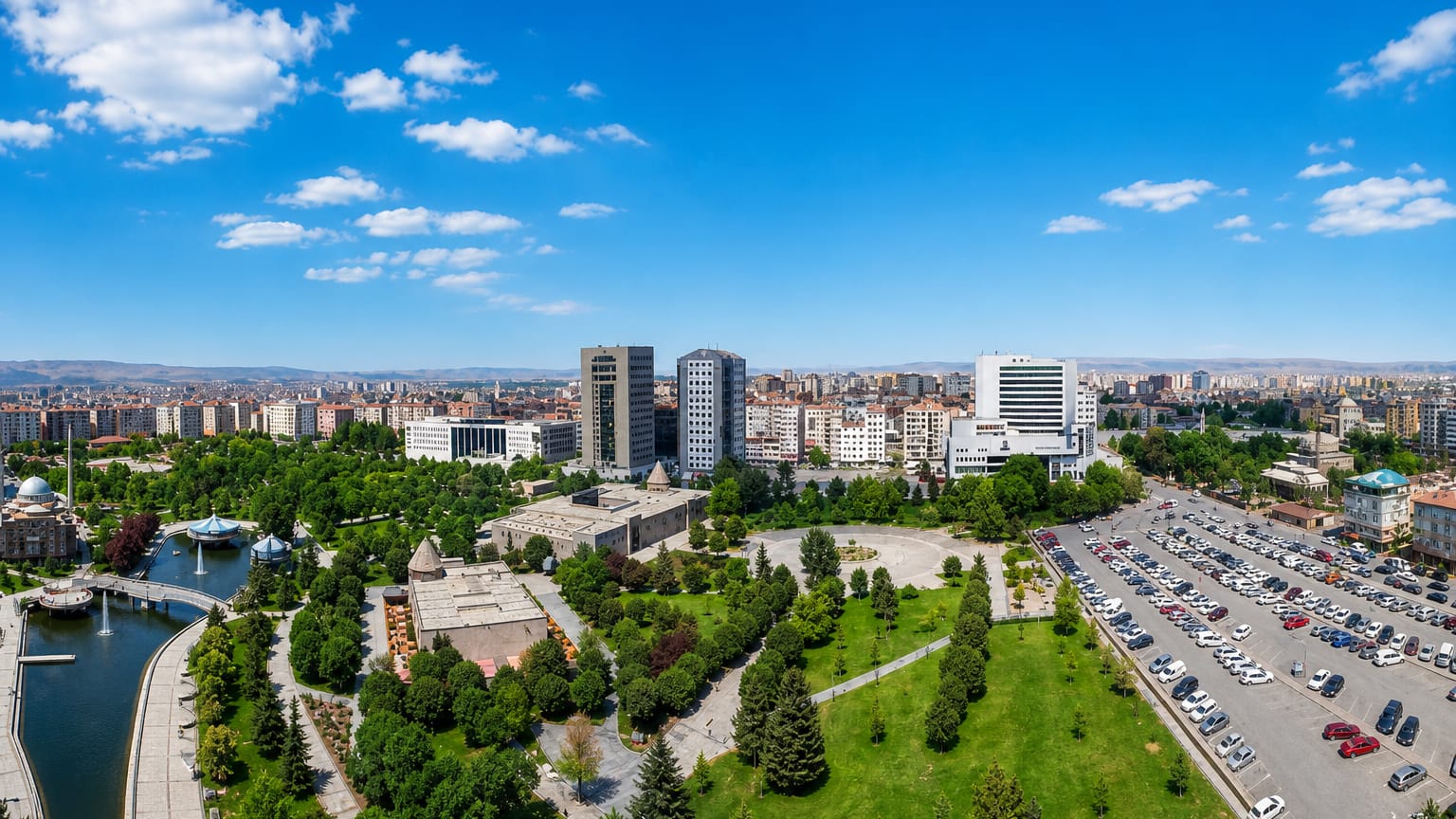 Aerial view of Kayseri with a green city park, pond and mid-rise towers spread toward distant mountains