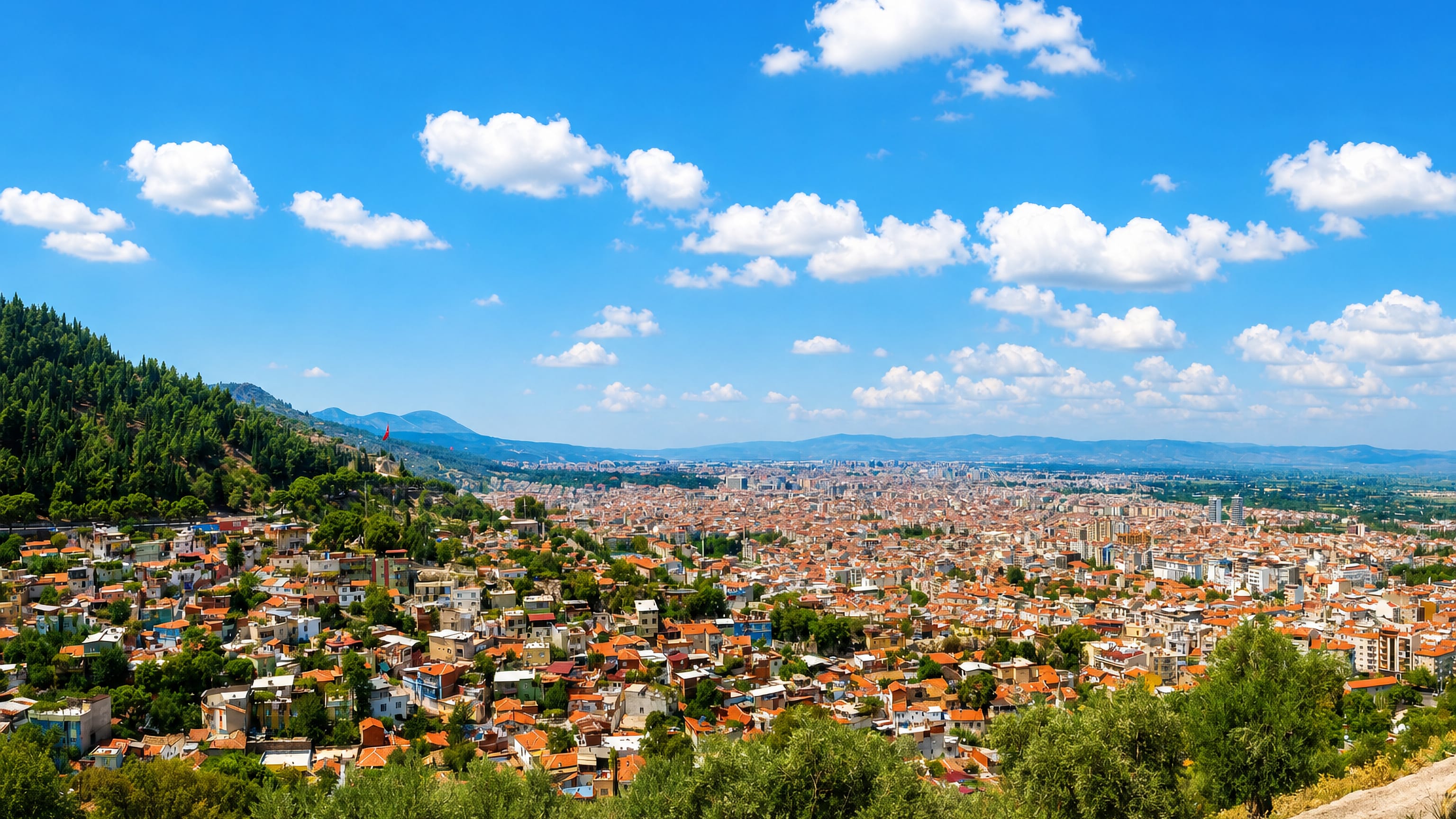 Manisa, Turkey spread across the plain below the wooded slopes of Mount Spil, red-tiled roofs in bright sun.
