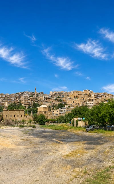 Mardin's terraced old town of honey-coloured stone houses stacked on a hillside under a bright blue sky