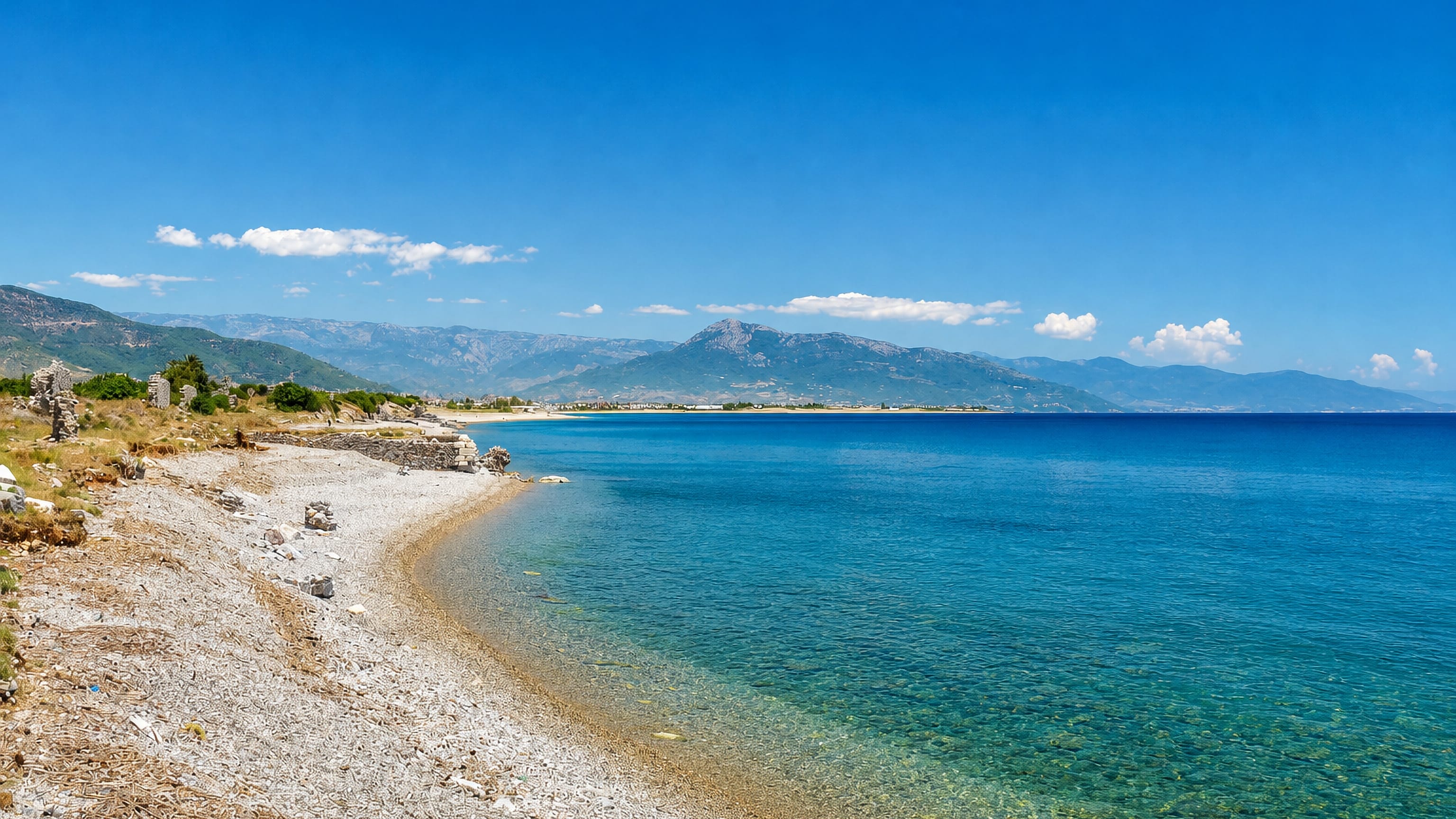 Pebble shoreline and turquoise Mediterranean water at Anamur on Turkey's Mersin coast, with mountains beyond.