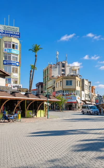 Sunny pedestrian square in Tarsus, Turkey, lined with market stalls, shops and a mosque minaret