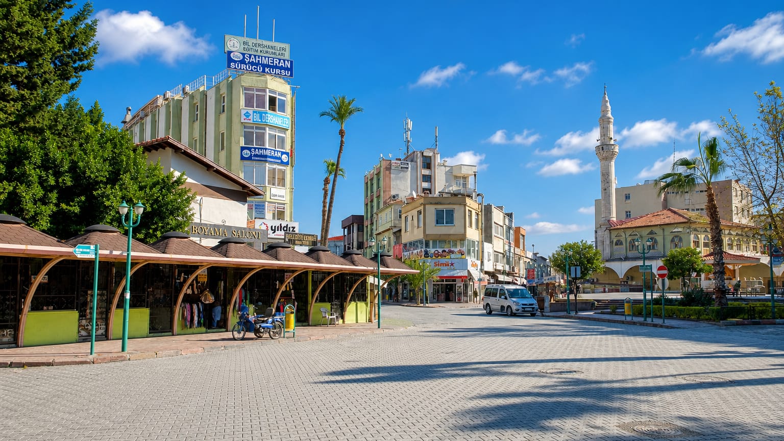 Sunny pedestrian square in Tarsus, Turkey, lined with market stalls, shops and a mosque minaret