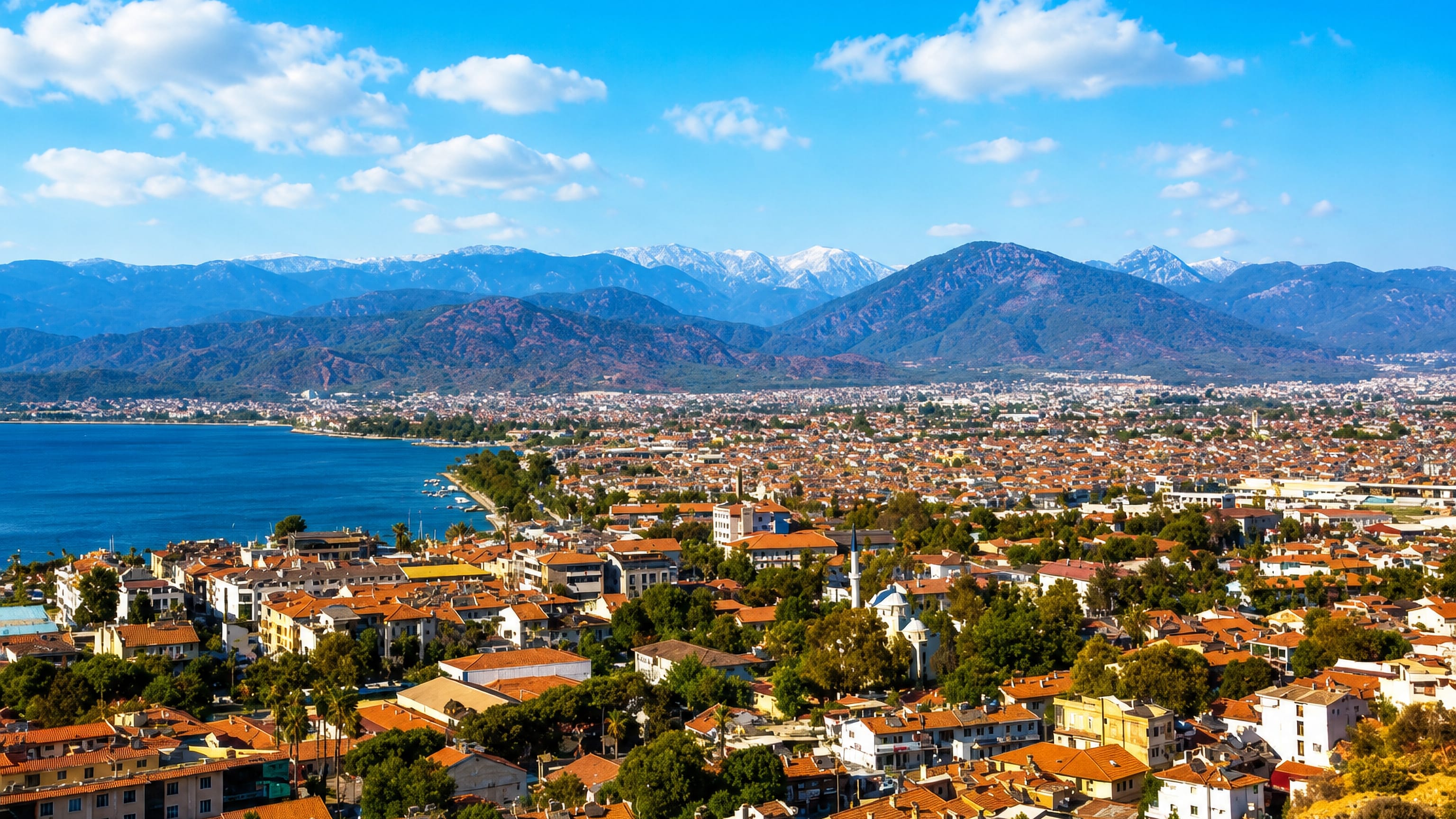 Hillside view over Fethiye's red-roofed town, mosque minaret and bay with the Taurus mountains behind.