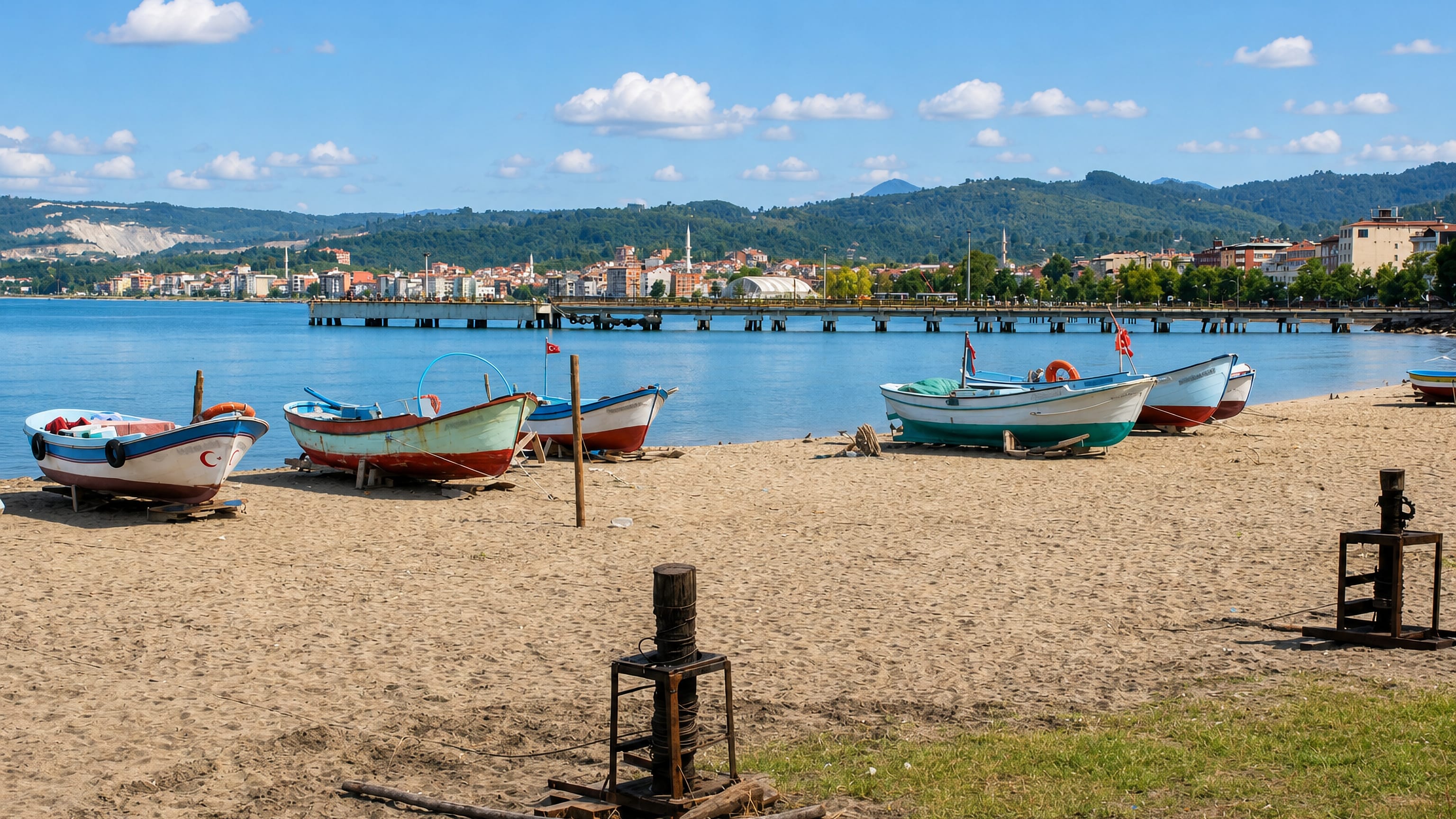 Fishing boats drawn up on the sand at Ünye, with the Black Sea town and green hills beyond the pier.