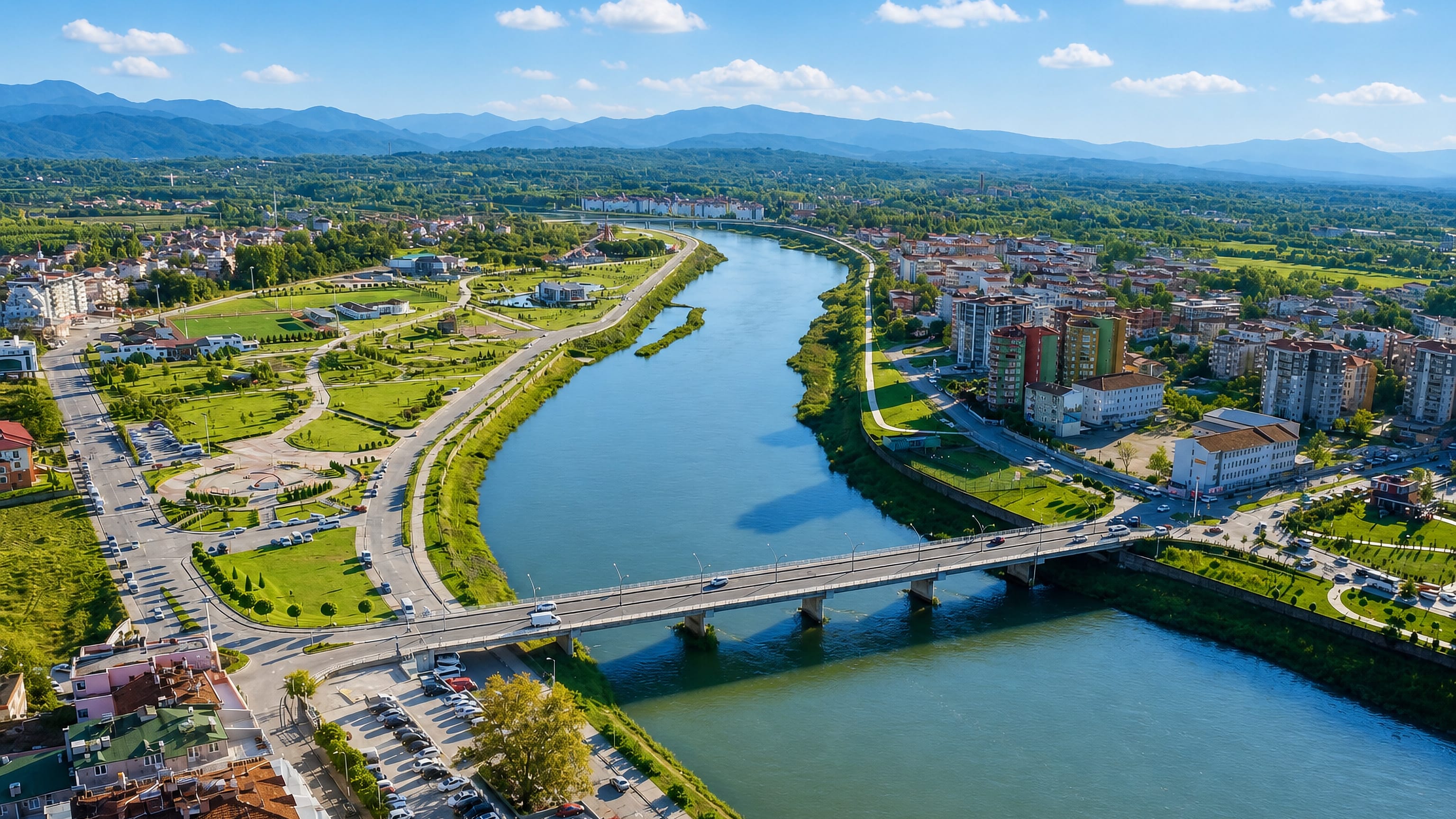 Aerial view of Çarşamba, Turkey, split by the Yeşilırmak river and its bridge, with hills beyond.