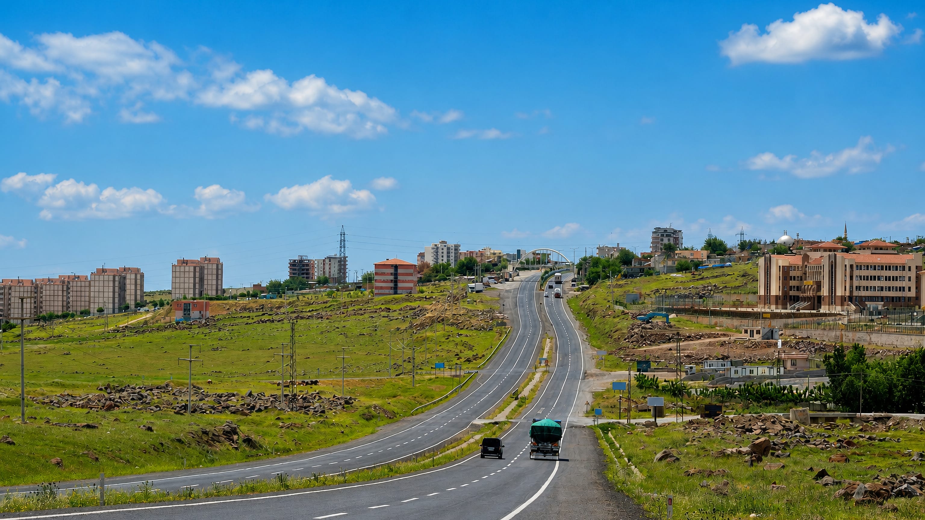 Highway approaching Siverek, Turkey, with apartment blocks and a mosque dome rising above basalt-strewn steppe.