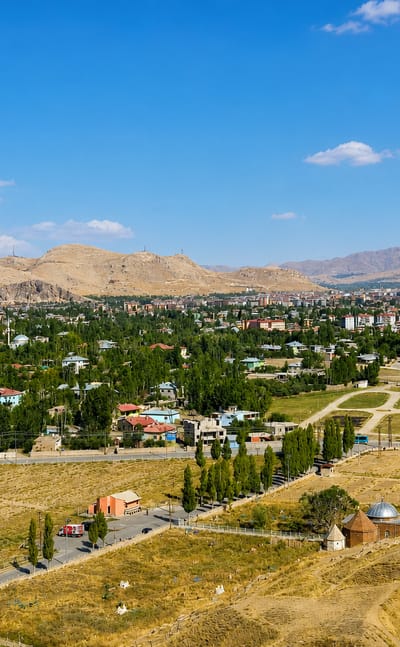 Wide daytime view over Van, Turkey, with a rocky castle ridge, low houses and distant arid mountains