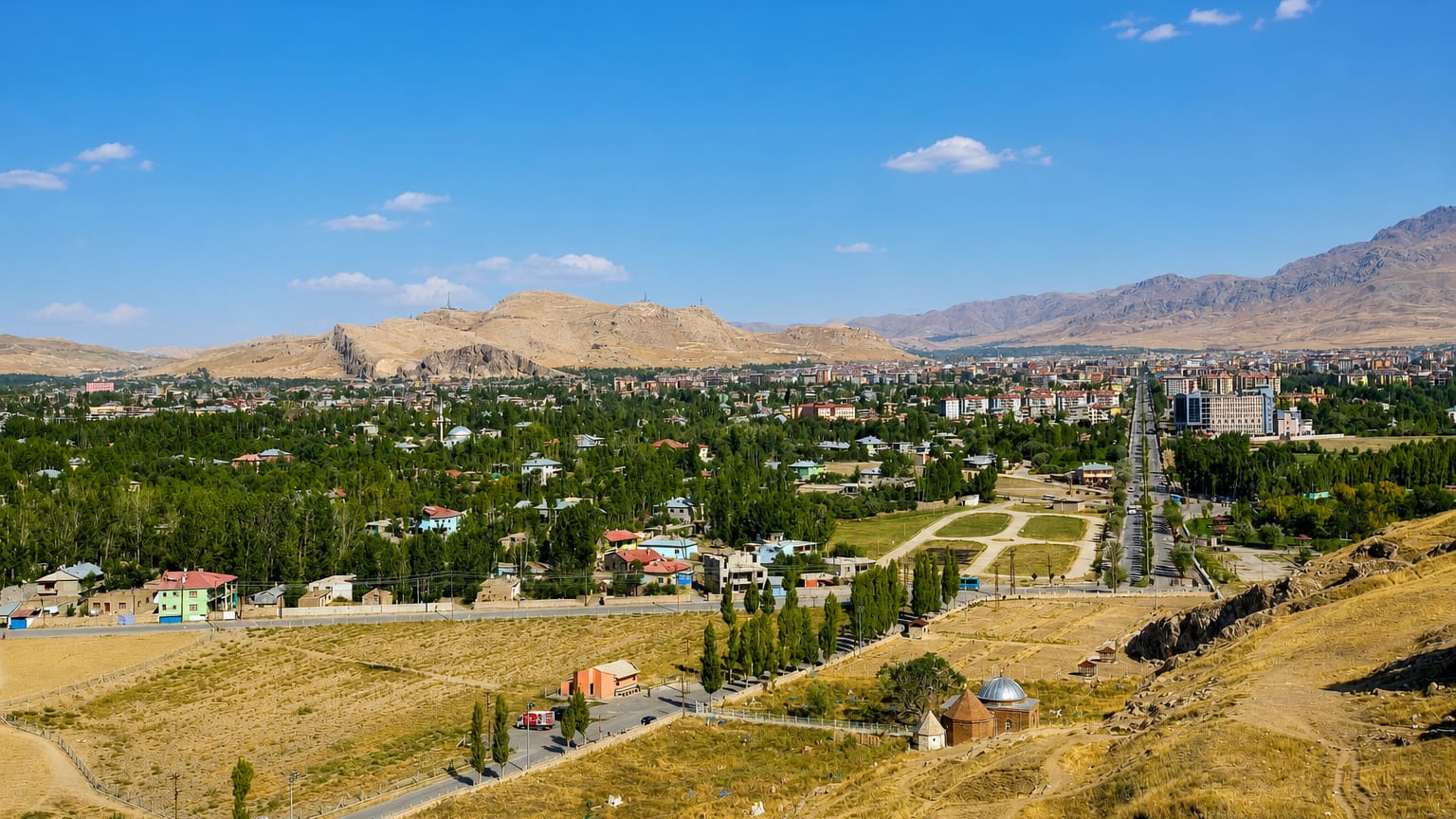 Wide daytime view over Van, Turkey, with a rocky castle ridge, low houses and distant arid mountains