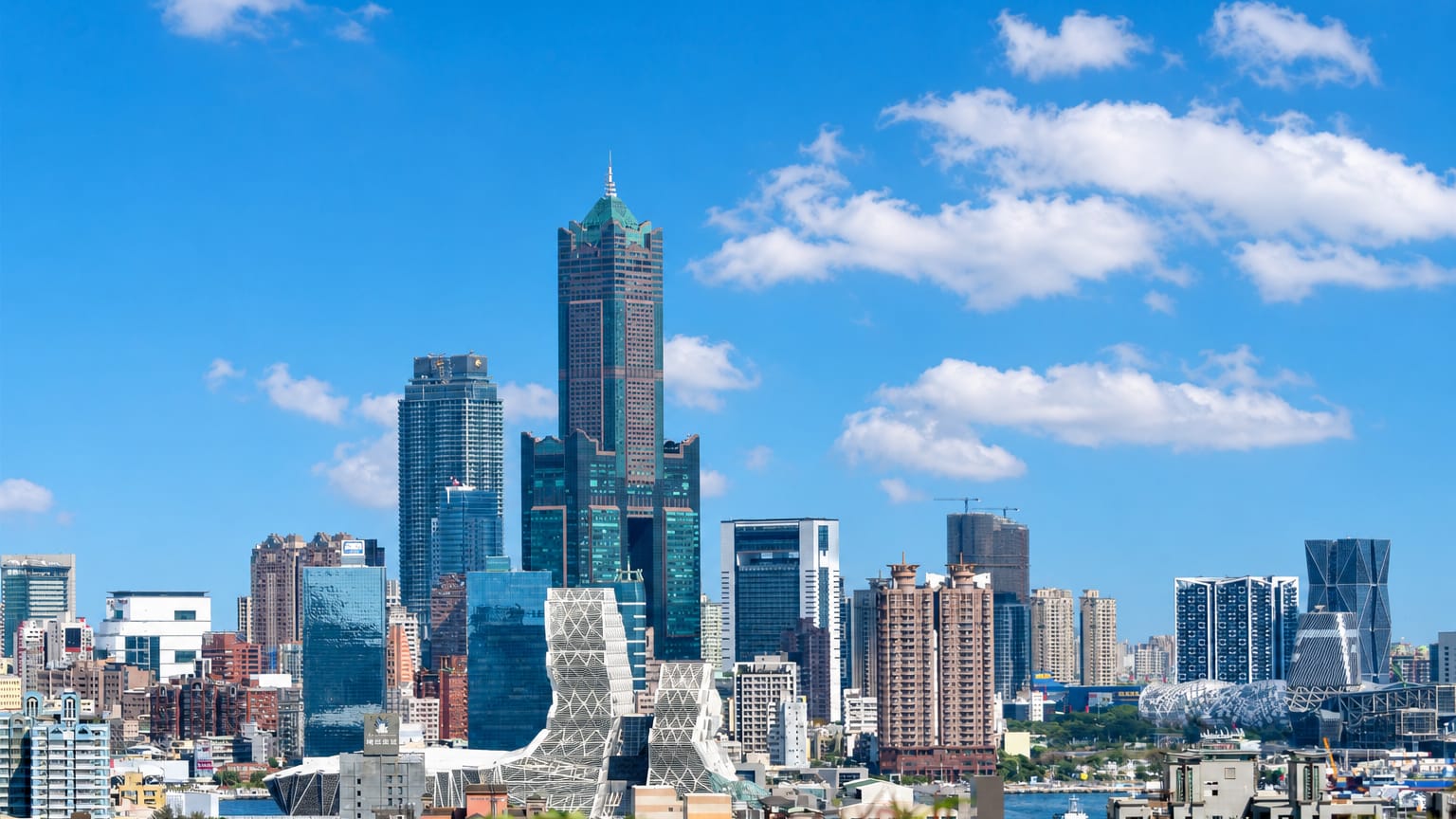 Kaohsiung skyline led by the 85 Sky Tower with the Music Center and harbour under a blue sky.
