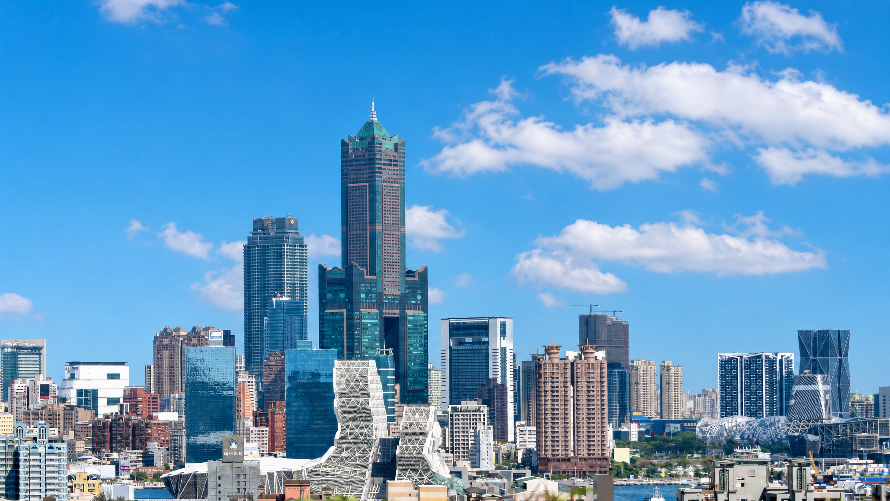 Kaohsiung skyline led by the 85 Sky Tower with the Music Center and harbour under a blue sky.