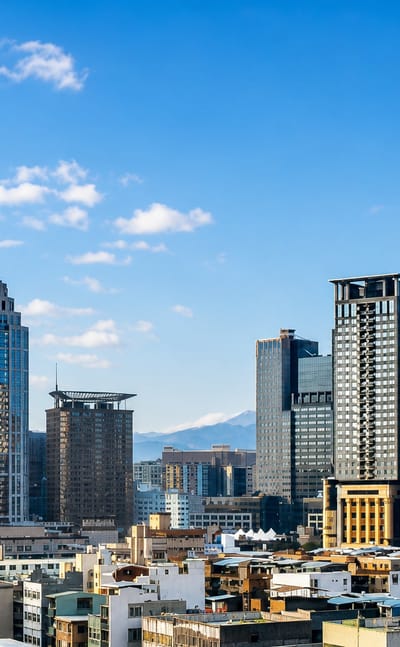 Skyline of high-rise towers in New Taipei City, Taiwan, with mountains rising behind under a clear sky