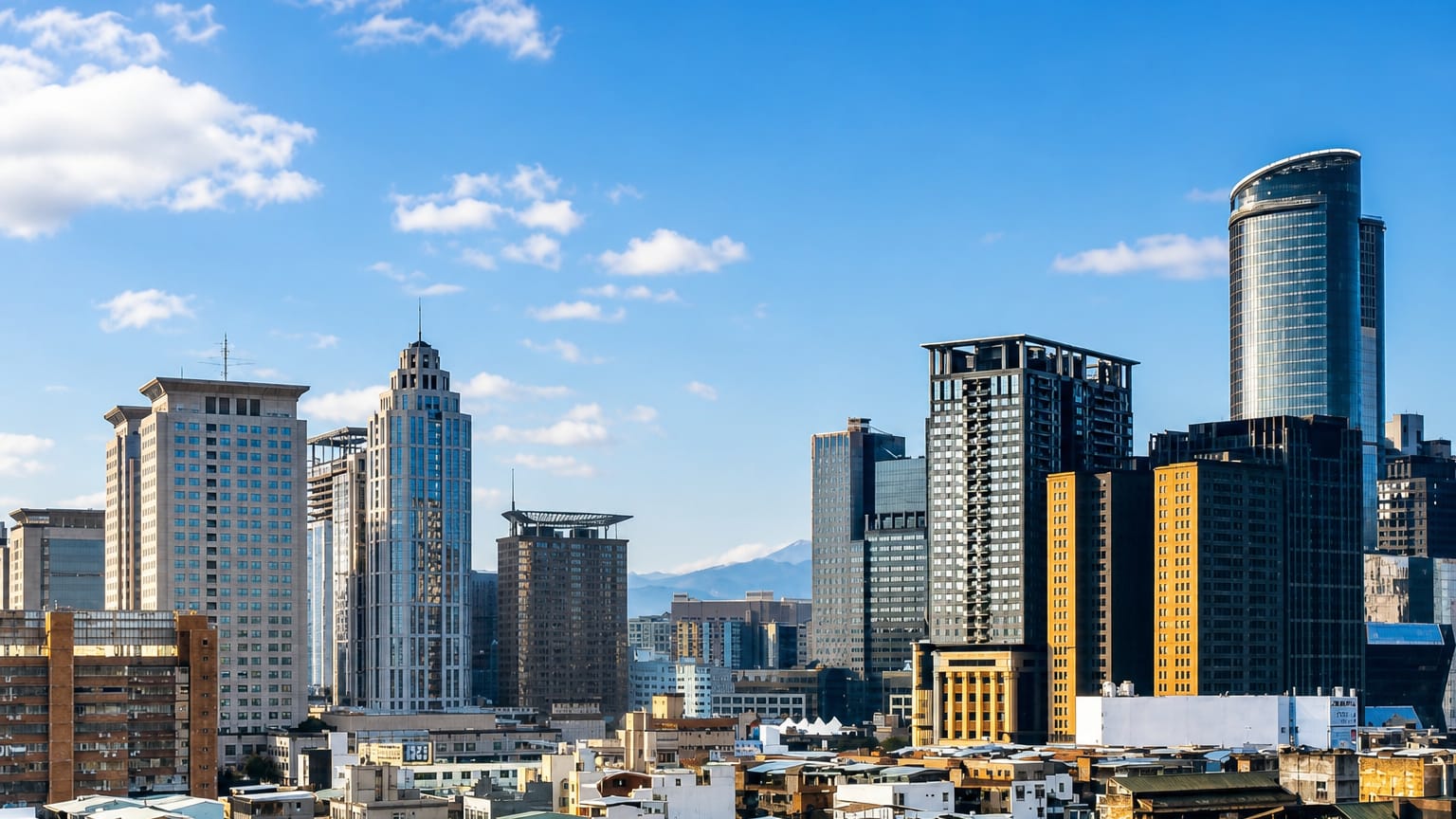 Skyline of high-rise towers in New Taipei City, Taiwan, with mountains rising behind under a clear sky