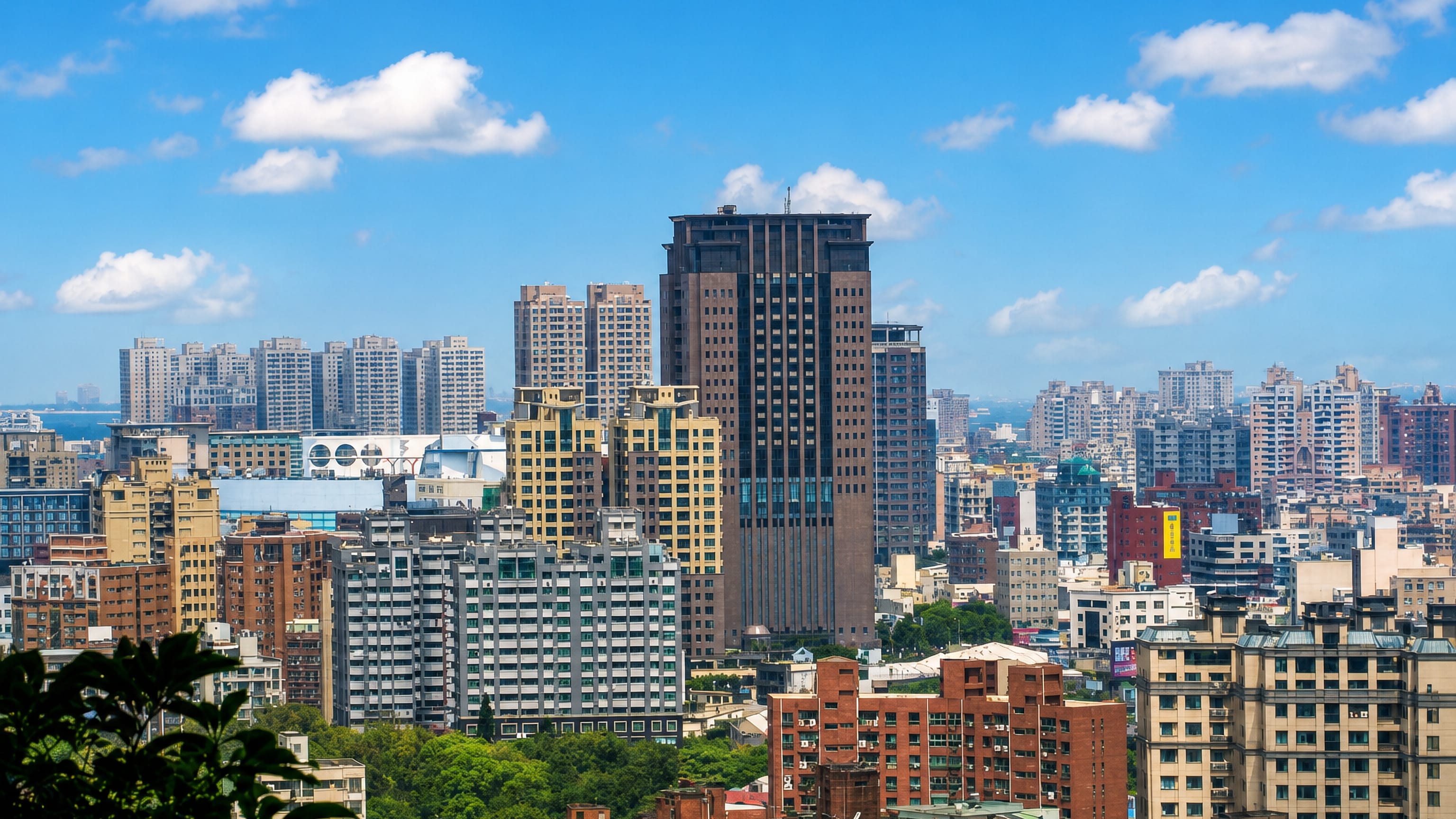 Dense high-rise apartment blocks and a dark office tower across the daytime skyline of Hsinchu, Taiwan.