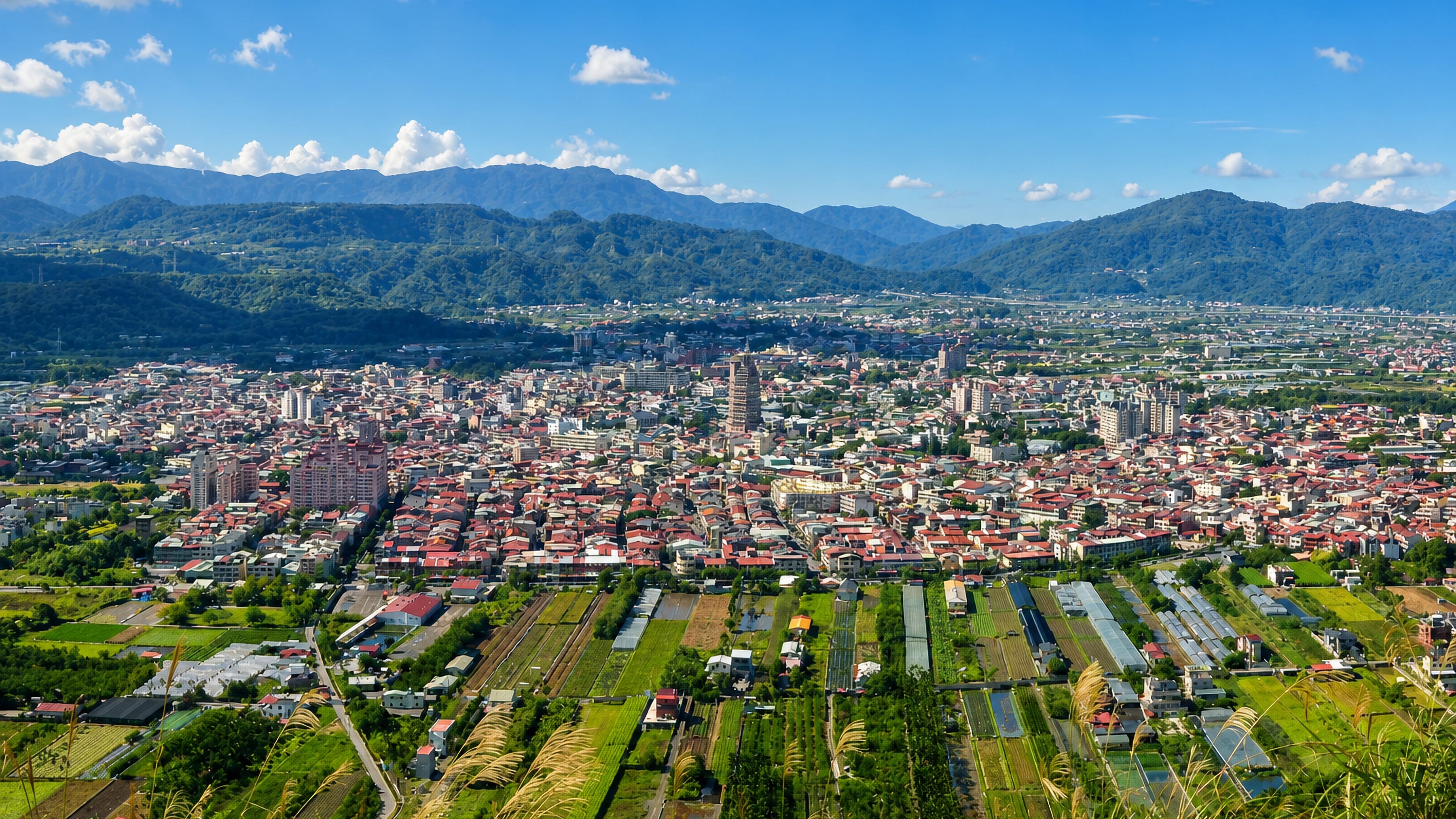 Puli town filling its mountain-ringed basin in Nantou, Taiwan, with farm plots and greenhouses in the foreground.