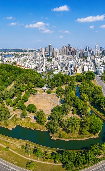Aerial view of Tainan, Taiwan, with a fort's green earthwork ramparts and canals before the modern city skyline