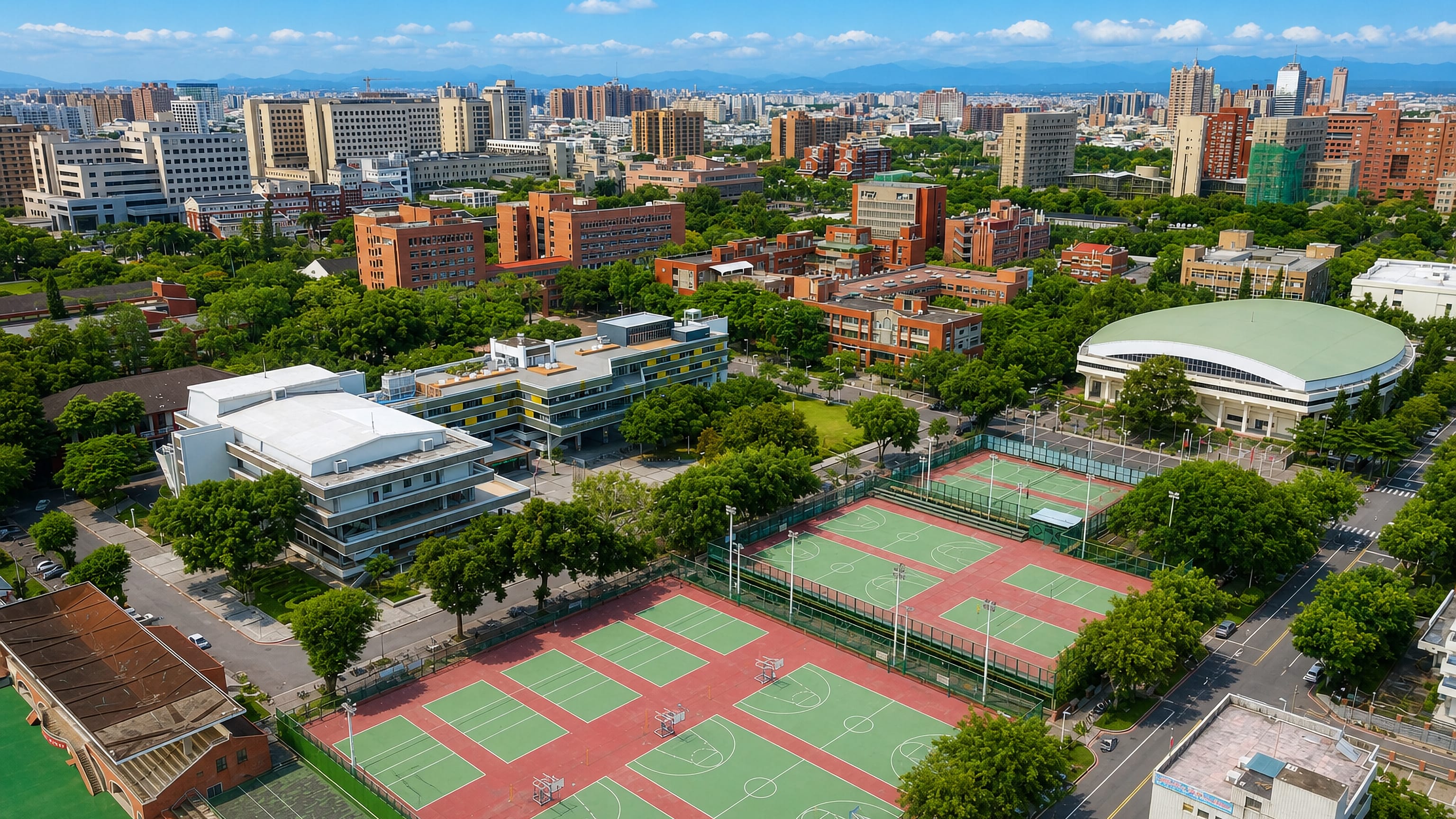 University sports courts and a domed gymnasium from above in Tainan's East District, city skyline beyond.