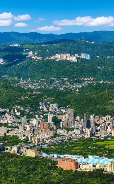 Aerial of low-rise Beitou nestled among green mountains with paddy fields in northern Taipei, Taiwan.