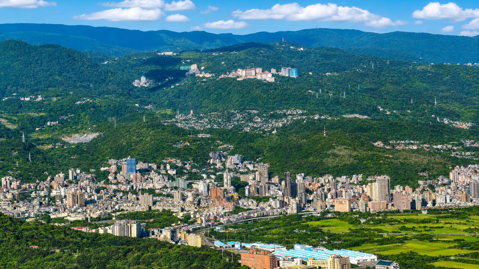 Aerial of low-rise Beitou nestled among green mountains with paddy fields in northern Taipei, Taiwan.