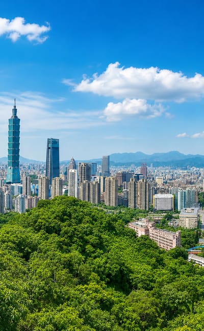 Taipei skyline seen over forested hills, with the tiered Taipei 101 tower rising above the city under a blue sky.