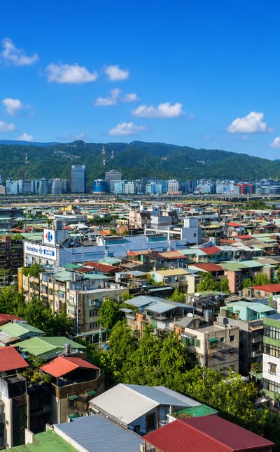 Aerial view of the dense low-rise urban fabric of Taipei's Neihu District beneath green mountains