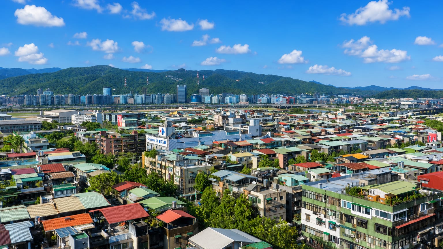Aerial view of the dense low-rise urban fabric of Taipei's Neihu District beneath green mountains