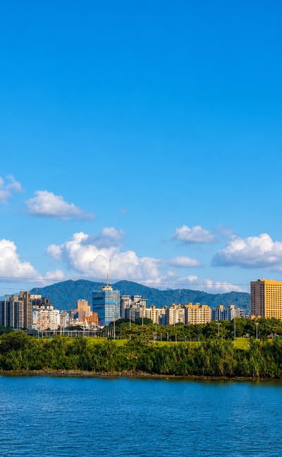 Riverside skyline of Taipei's Wanhua District with Taipei 101 rising beyond a tree-lined riverbank