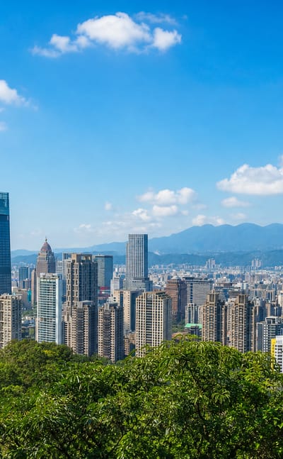 Taipei skyline with Taipei 101 towering over the Xinyi District high-rises, viewed from a green hillside.