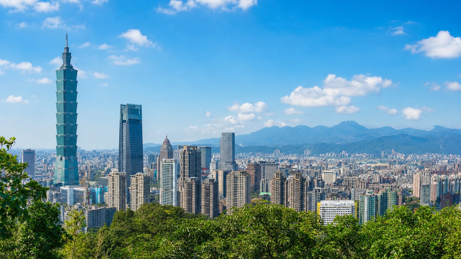 Taipei skyline with Taipei 101 towering over the Xinyi District high-rises, viewed from a green hillside.
