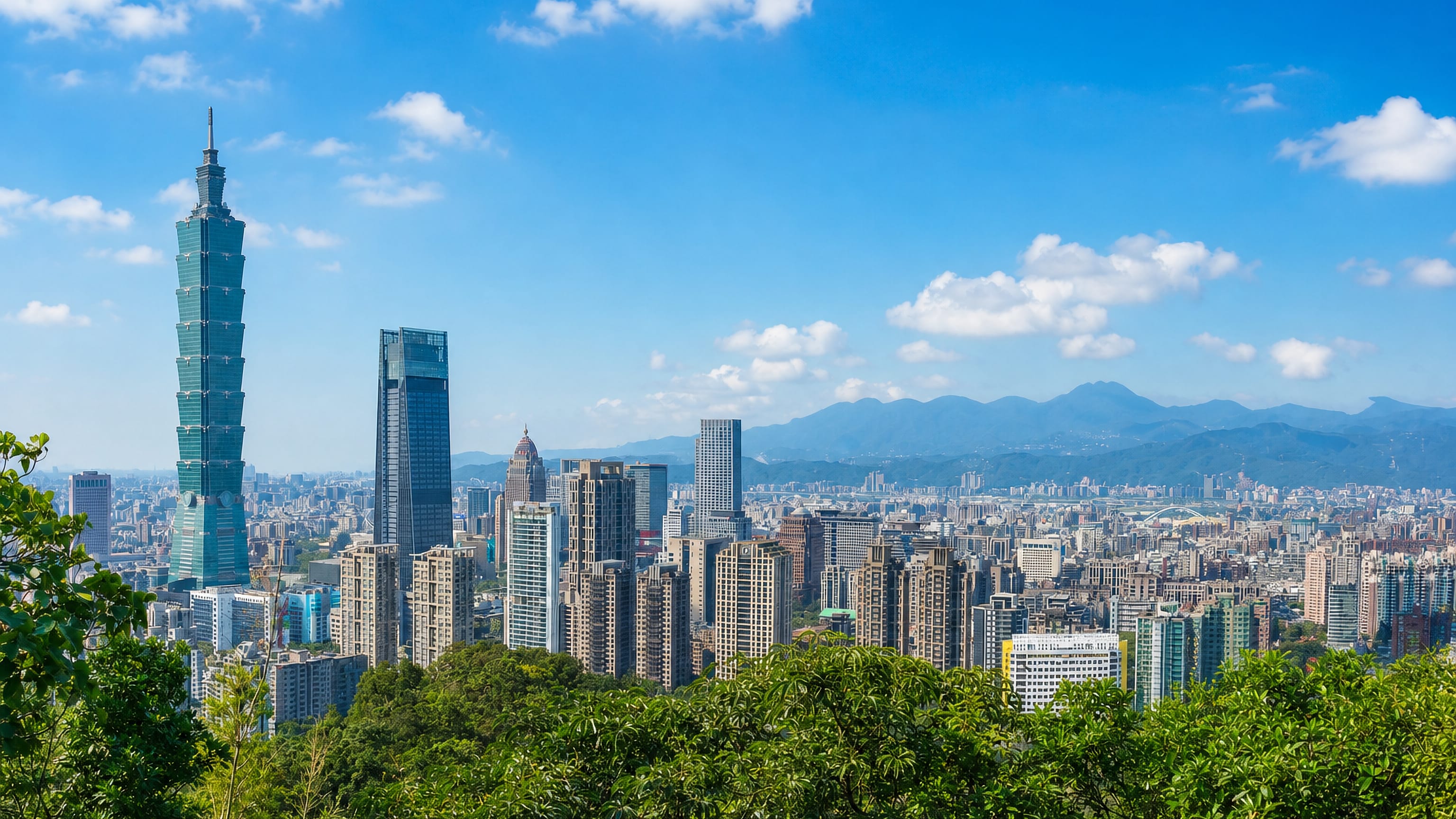 Taipei skyline with Taipei 101 towering over the Xinyi District high-rises, viewed from a green hillside.