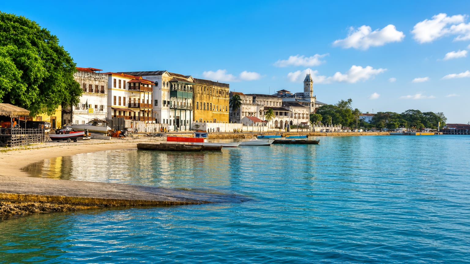 Zanzibar Stone Town seafront, Tanzania, with historic buildings, a clock tower and boats on turquoise water.