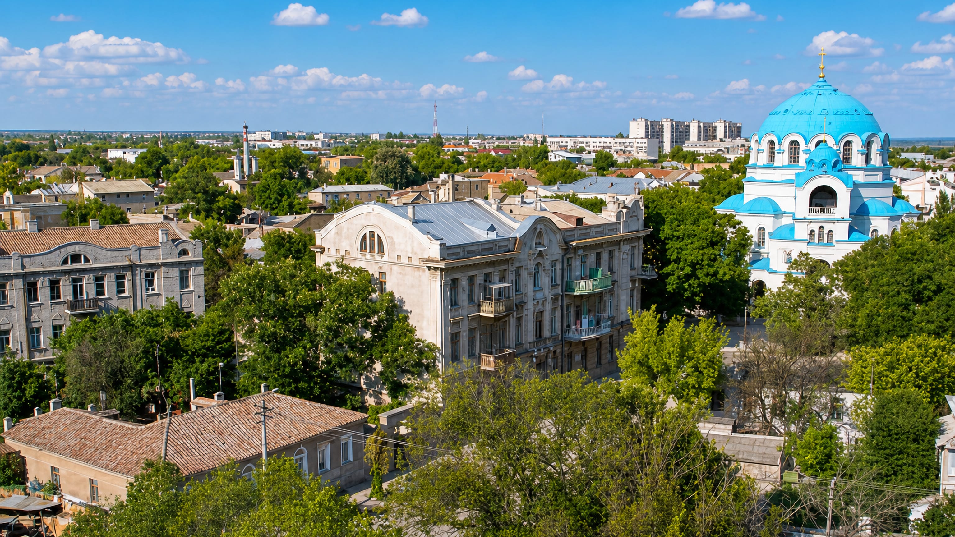 Rooftops of Yevpatoriya, Crimea, with the blue domes of St Nicholas Cathedral rising above leafy streets.