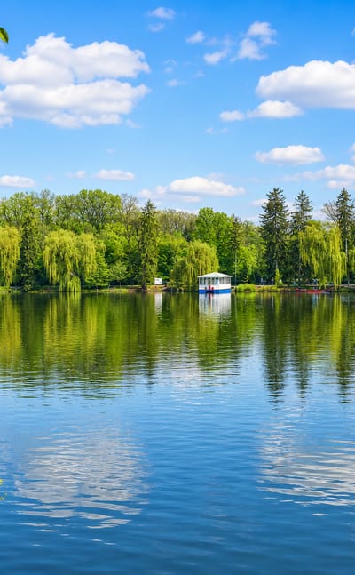 Tree-lined lake with willows and a small pleasure boat in Sofiyivka Park, Uman, under a blue sky