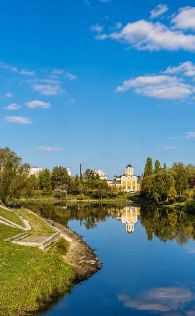 Riverside park in Chernihiv, Ukraine, with a white golden-domed church reflected in a calm pond among autumn trees